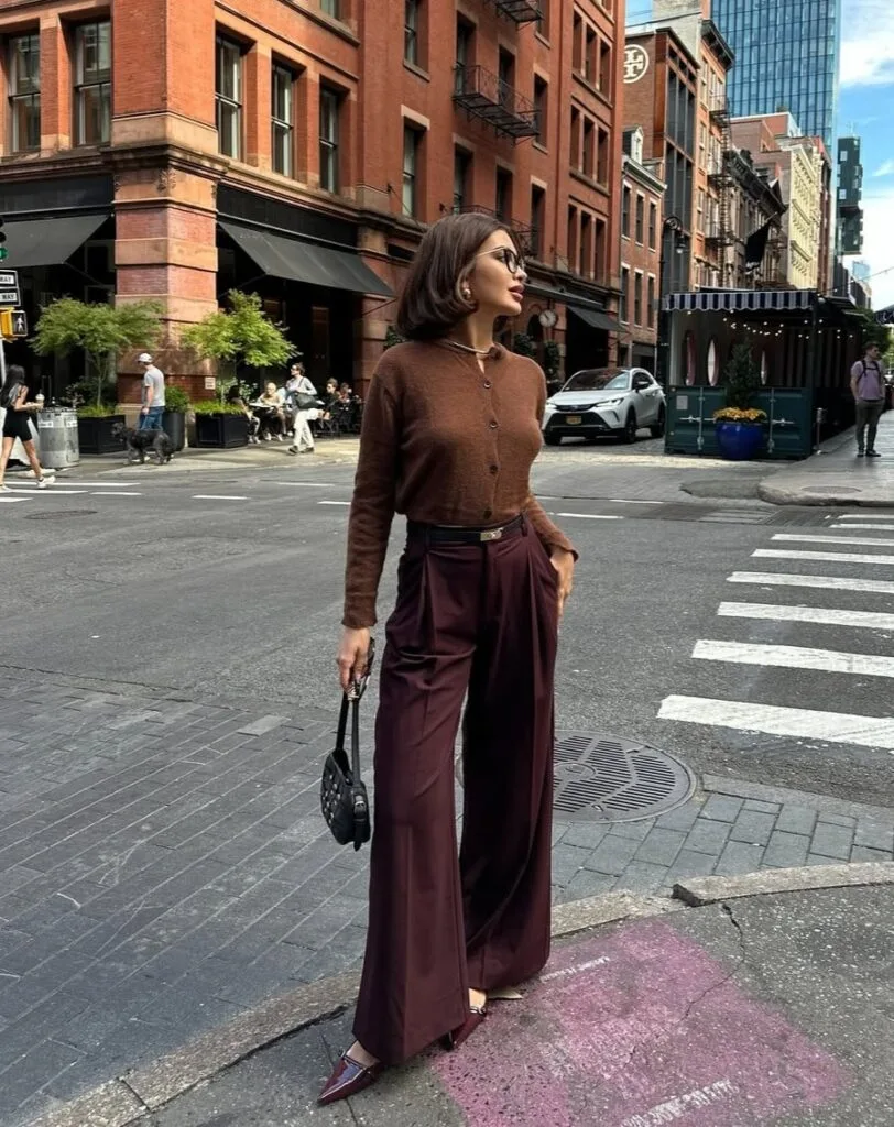 Woman in brown cardigan and burgundy wide-leg pants, crossing city street; chic fall business casual outfit.

