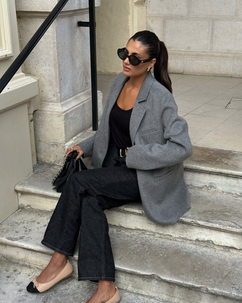  Woman in grey blazer, black jeans, black top, and ballet flats, sitting on steps; fall business casual style.