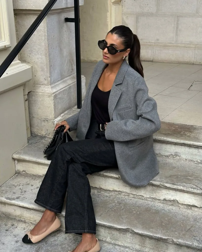  Woman in grey blazer, black jeans, black top, and ballet flats, sitting on steps; fall business casual style.