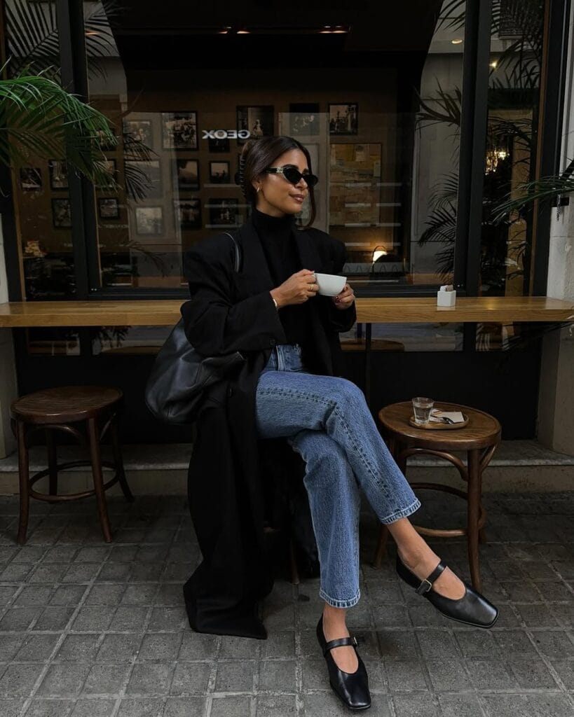 Fall outfit with long black coat, black turtleneck, blue jeans, and mary jane shoes