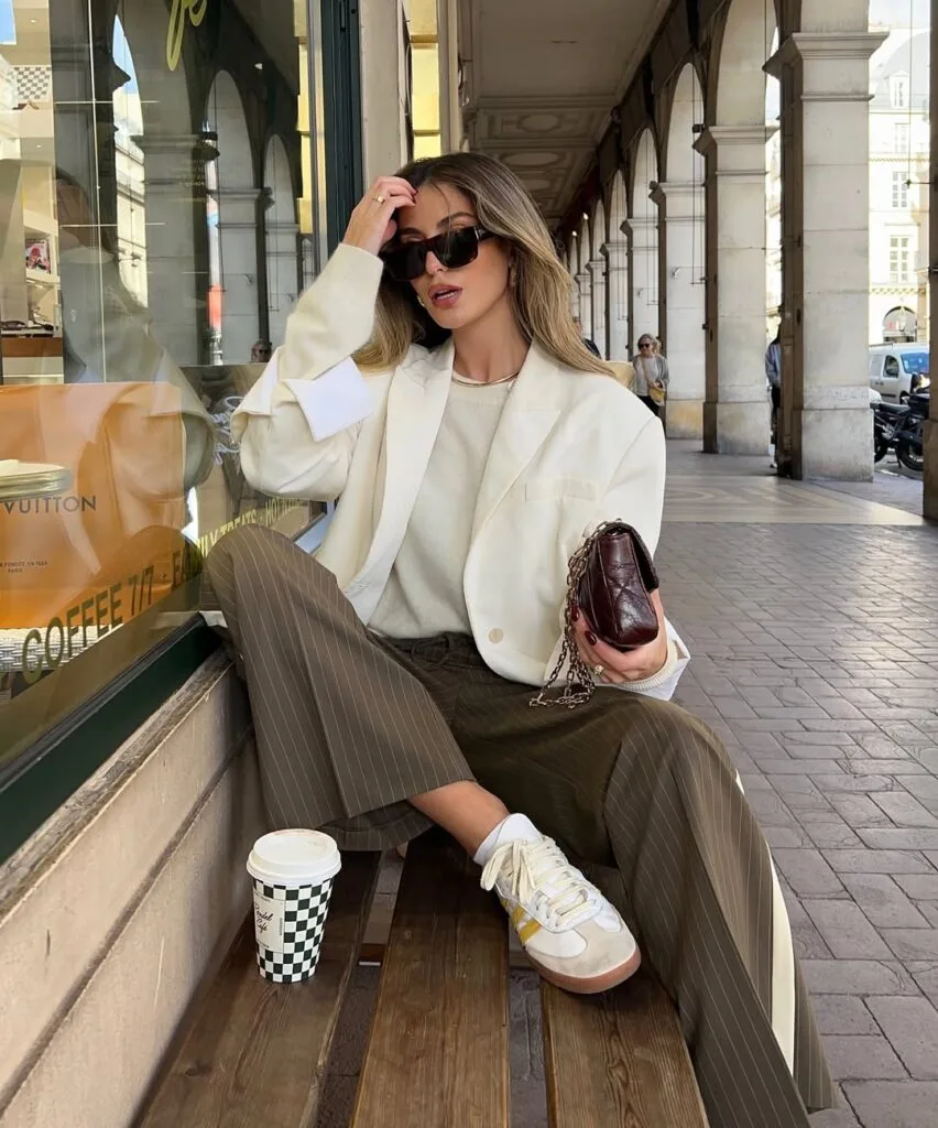 Woman in white blazer, sweater, and brown pinstripe pants with sneakers; business casual look for fall.