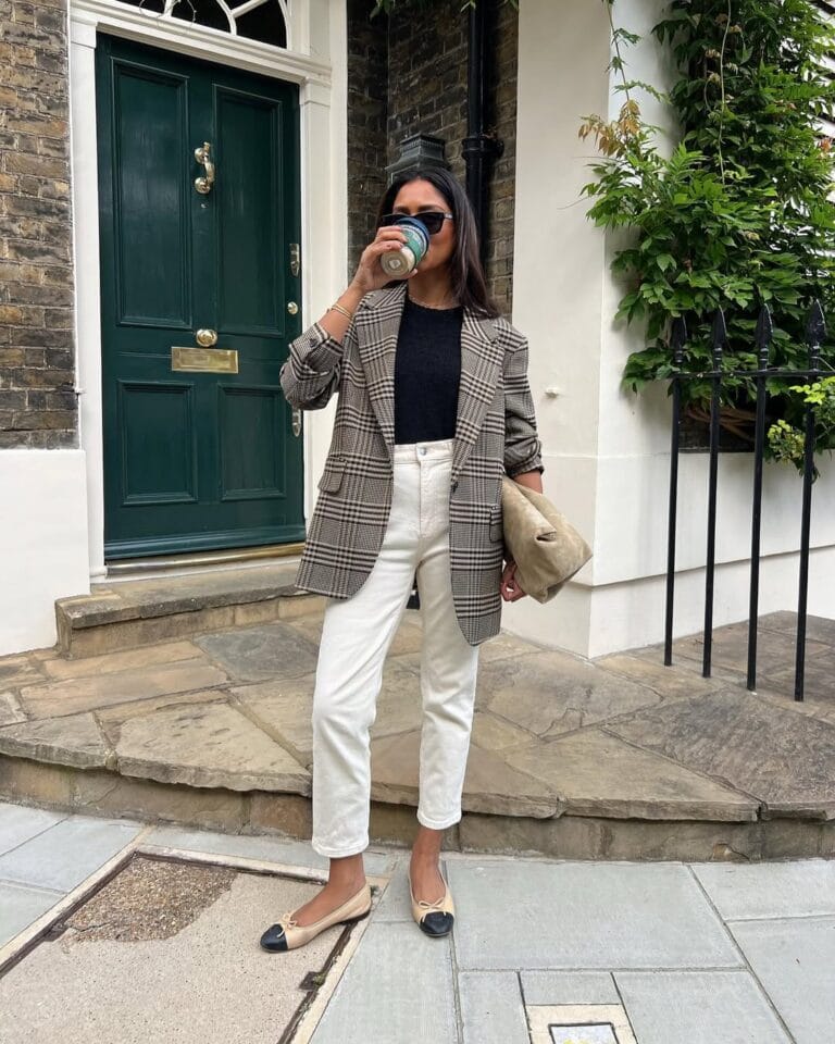 Woman in plaid blazer, white jeans, and black tee, drinking coffee; business casual outfit for fall.