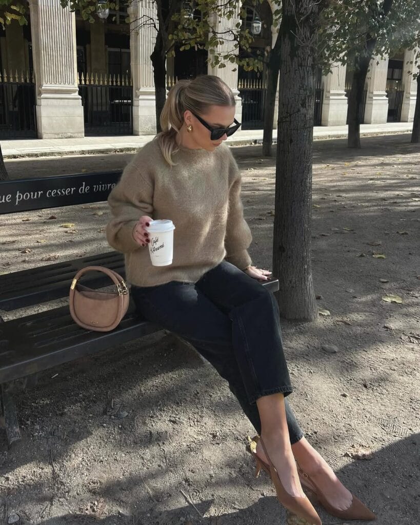 Woman in taupe fuzzy sweater and black jeans with caramel heels; cozy fall business casual outfit on bench.