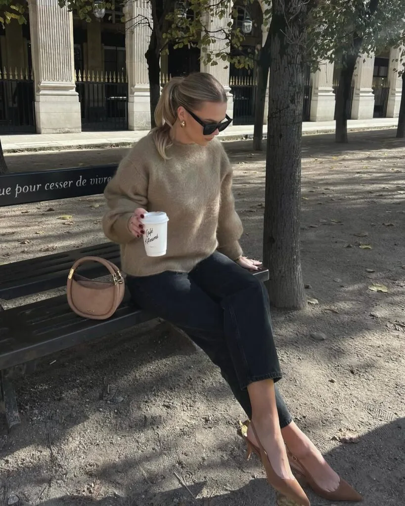 Woman in taupe fuzzy sweater and black jeans with caramel heels; cozy fall business casual outfit on bench.