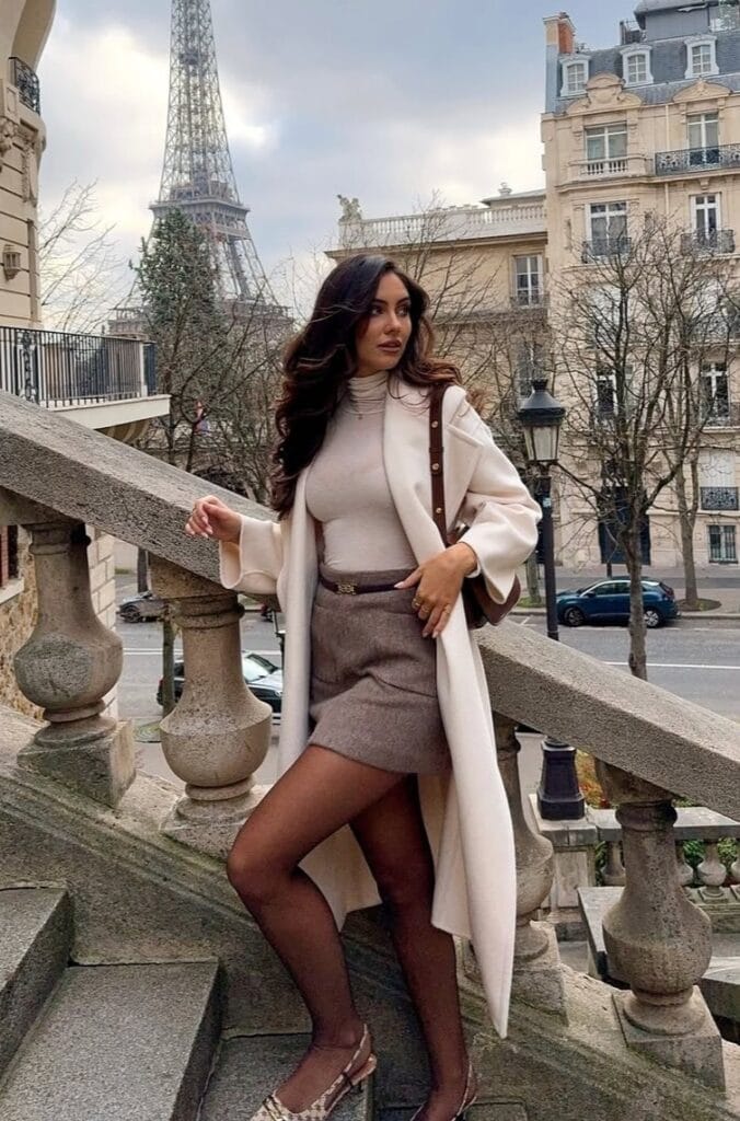 Classy fall outfit with cream long coat, grey mini skirt, tights, and heels