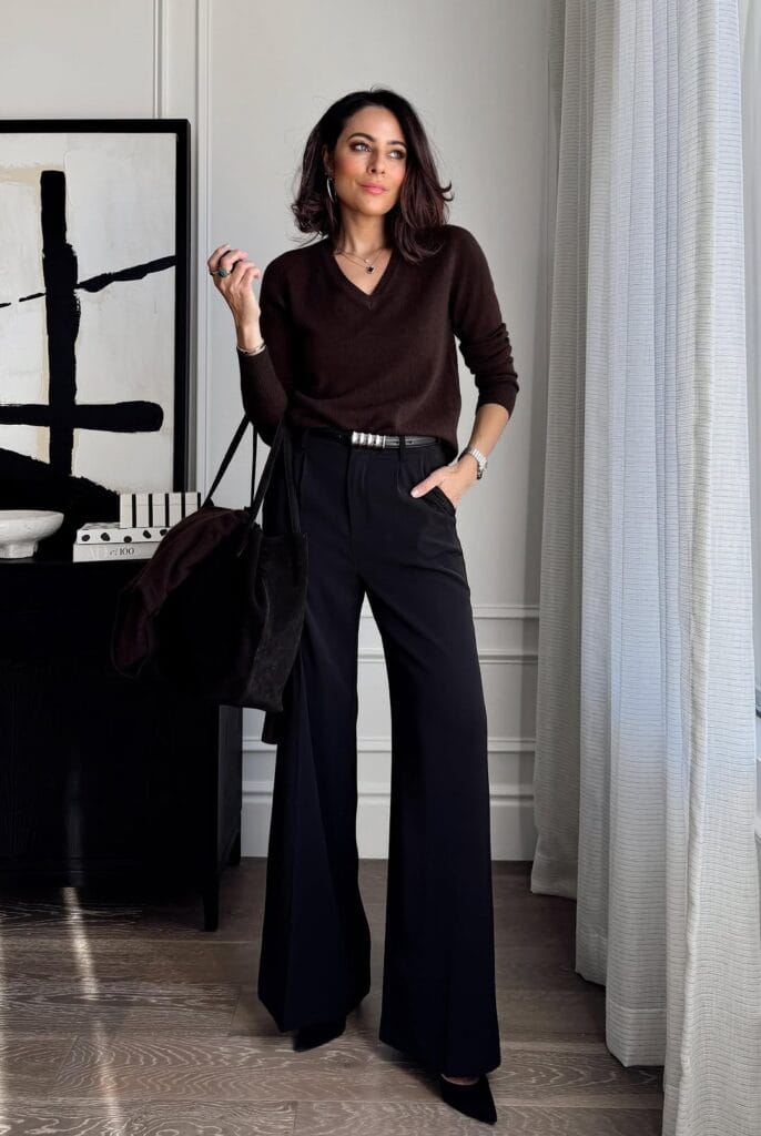 Woman in brown v-neck sweater and black wide-leg pants, holding black tote; elegant business casual outfit.
