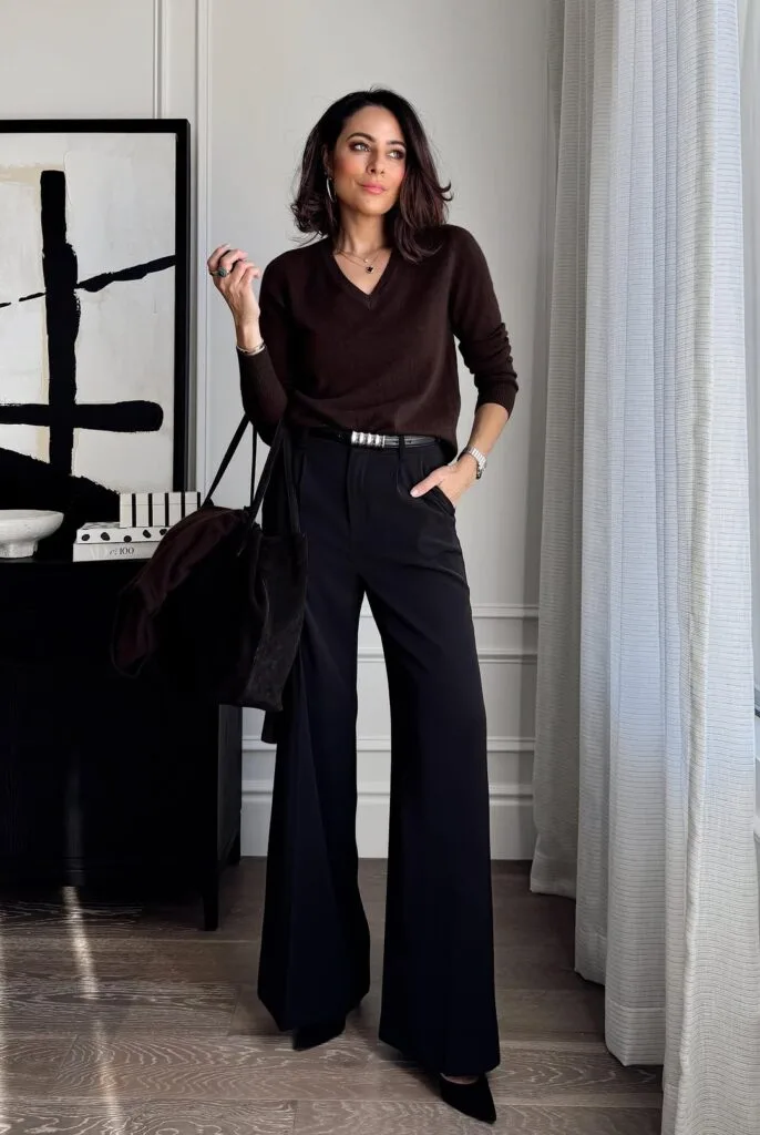Woman in brown v-neck sweater and black wide-leg pants, holding black tote; elegant business casual outfit.
