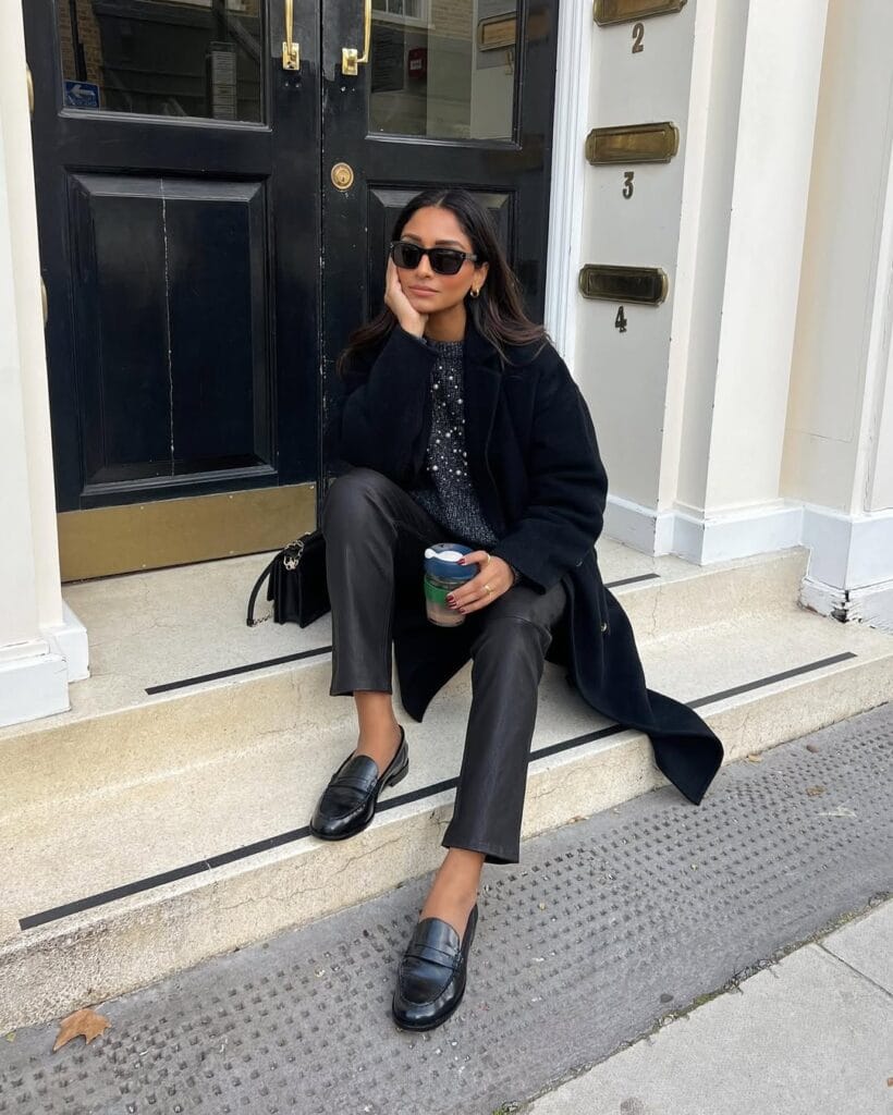Classy fall outfit with black coat, sequin top, leather pants, and black loafers