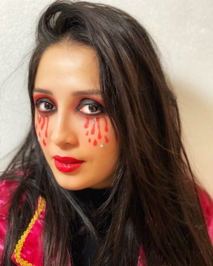 Halloween makeup with red “bloody tears” under smoky eyes and glossy red lips.