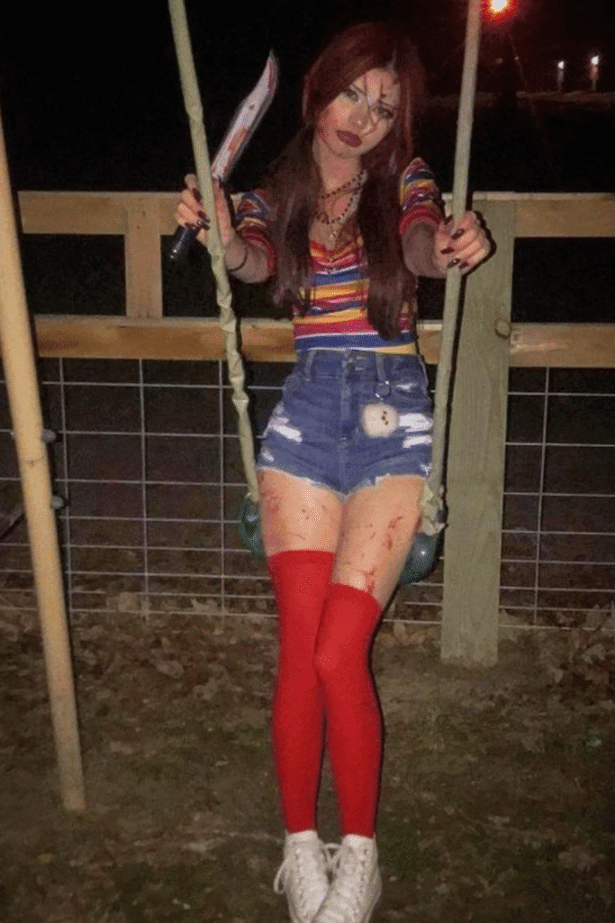 Chucky Halloween costume with rainbow shirt, denim shorts, red stockings, and scary doll makeup—a creepy-cute party look.
