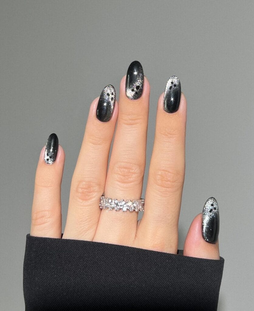 Black Halloween nails with silver glitter ombre and ghost face accents on almond shape.