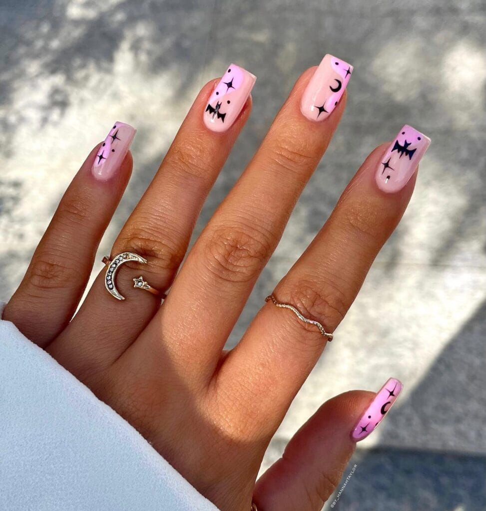 Pastel pink square nails with black bat, star, and moon nail art for Halloween.