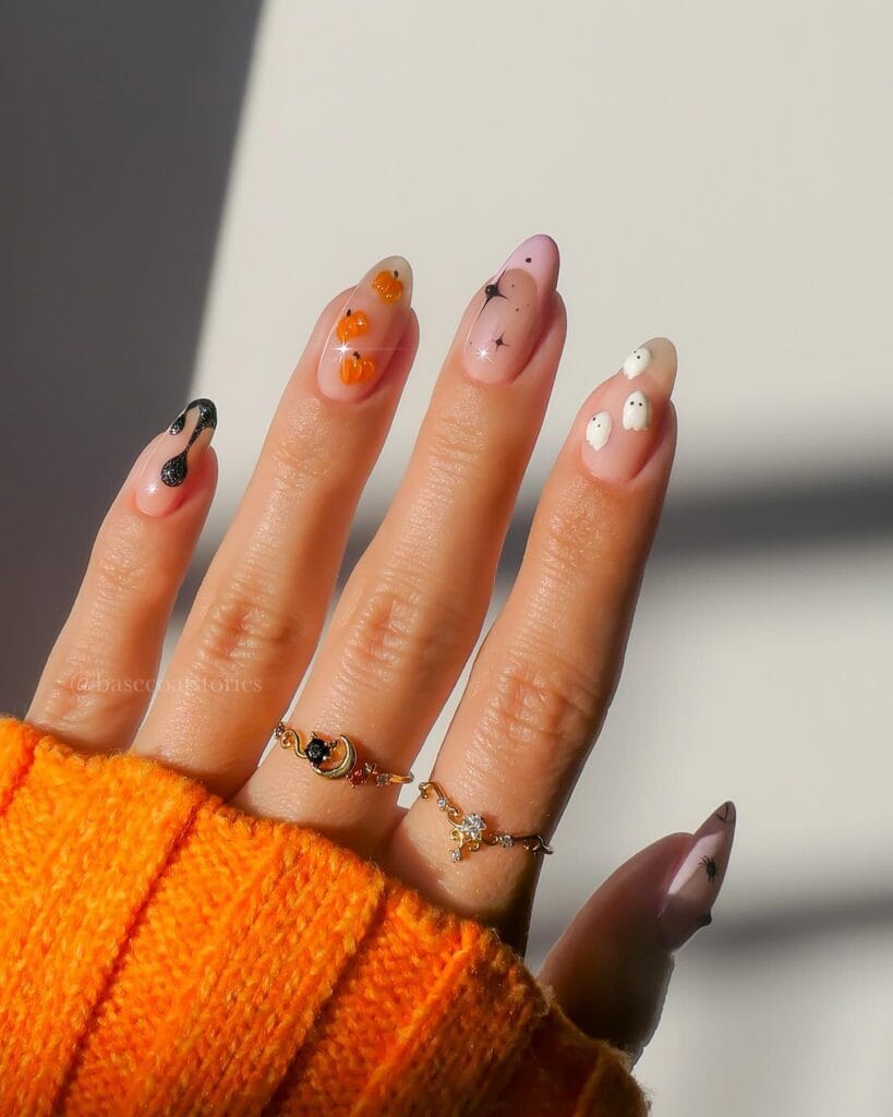 Nude Halloween nails with pumpkins, ghosts, black details, and stars on almond-shaped nails.
