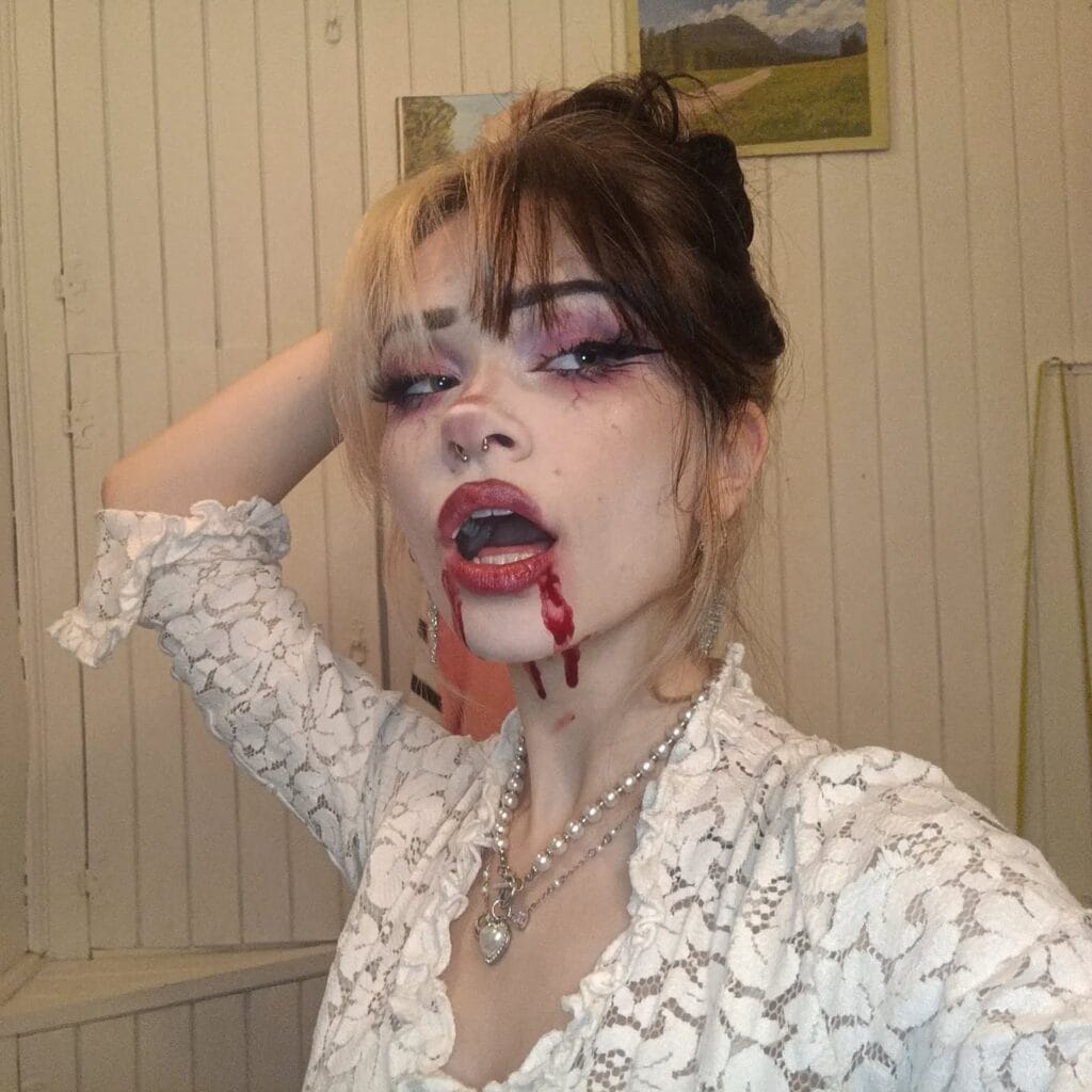 Vampire-inspired Halloween makeup with blood dripping from lips and smoky burgundy eyes.