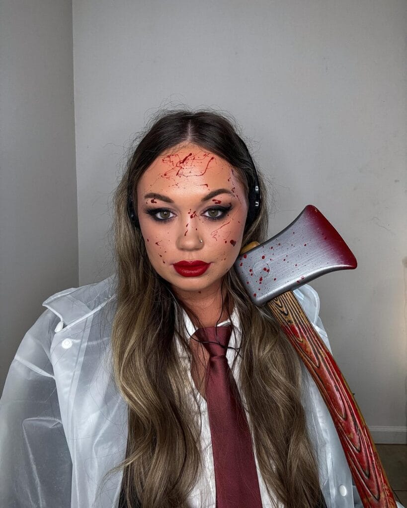 Halloween makeup with fake blood splatters and an axe accessory for a psycho killer