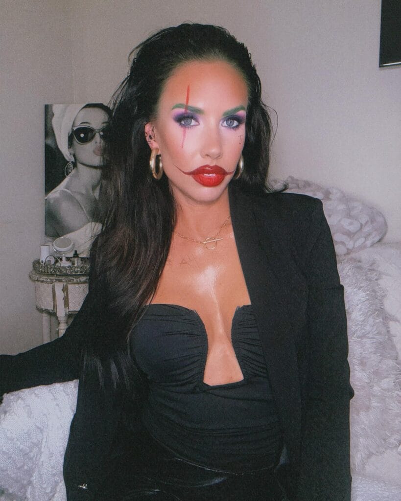 Joker-inspired Halloween makeup with rainbow eyeshadow and dramatic red lips and scars.