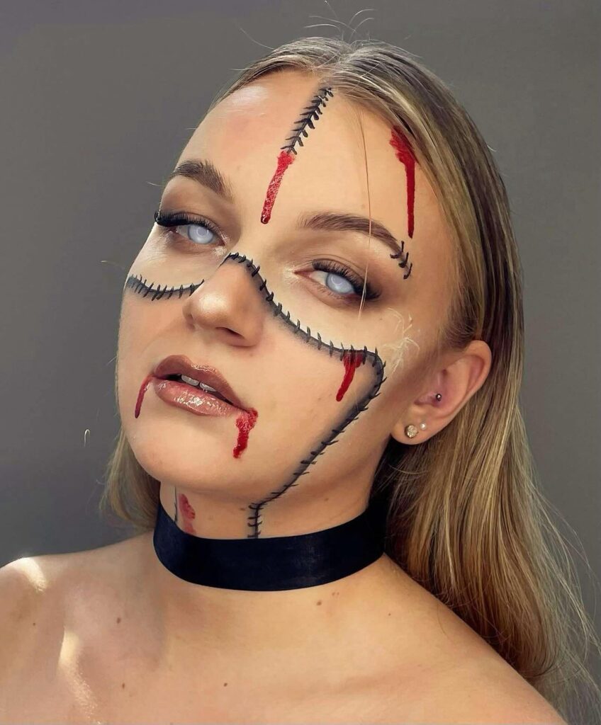 Halloween makeup with black stitches, white eyes, and bloody cuts for a stitched doll effect.