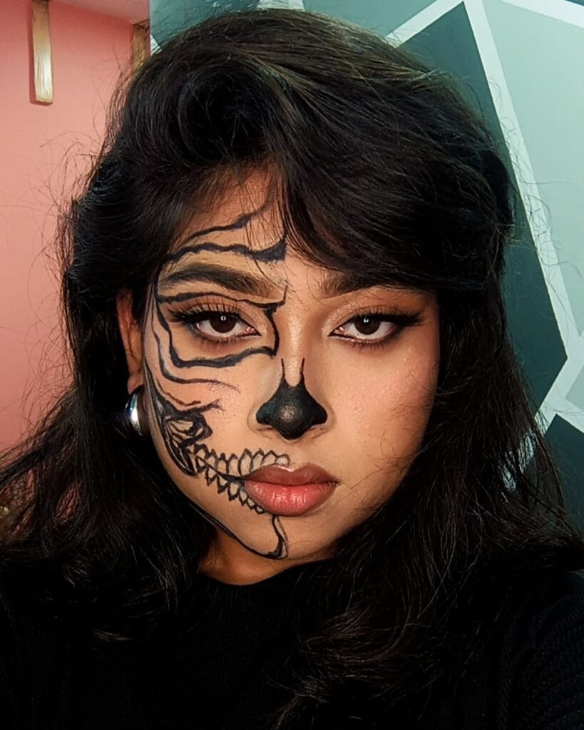 Halloween makeup with half-face black skeleton design and bold contouring.