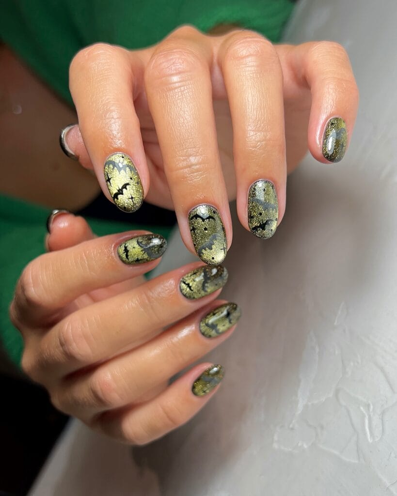 Black-green shimmer Halloween nails with gold clouds and bat nail art.

