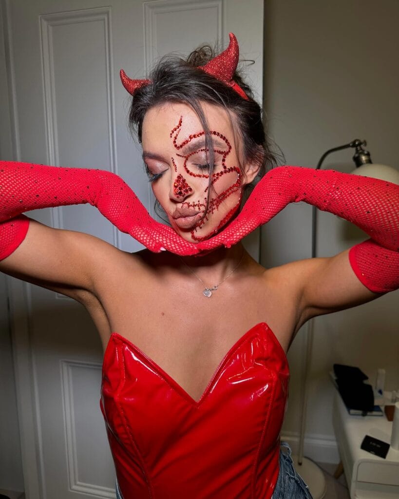 Halloween makeup with red rhinestones in a skull pattern and devil horns headband.