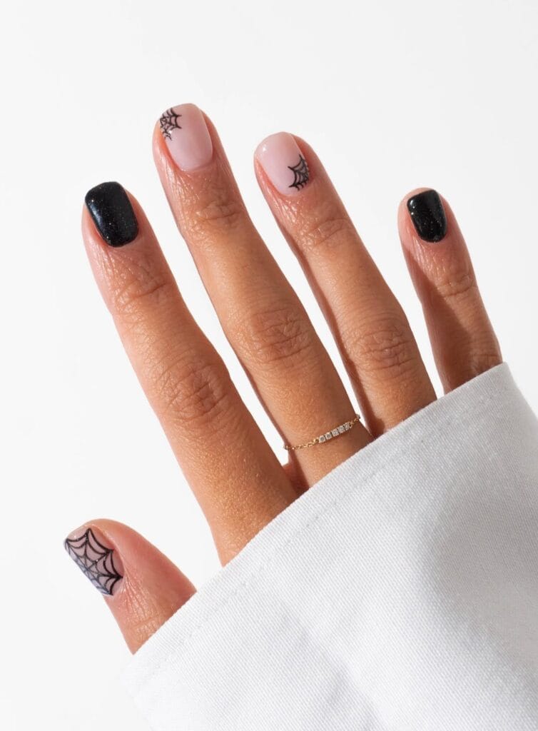 Black glitter and nude nails with simple spiderweb nail art for Halloween.