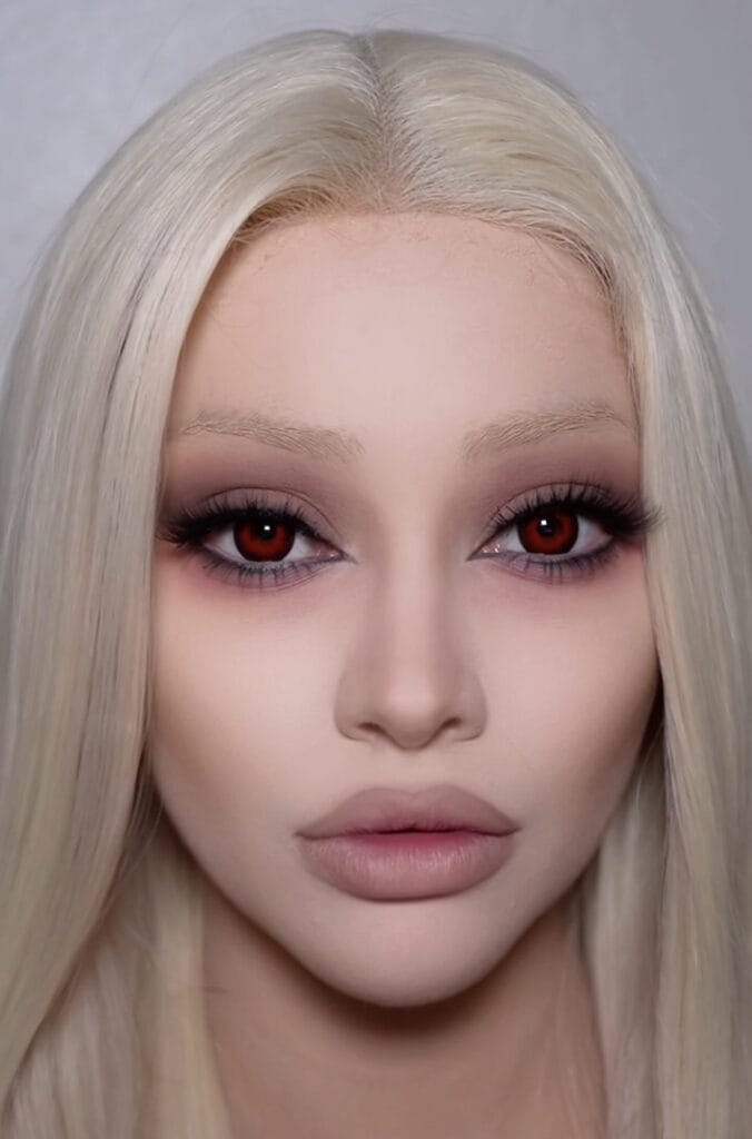 Halloween makeup with pale skin, smoky mauve eyes, and red contacts for a living doll look.