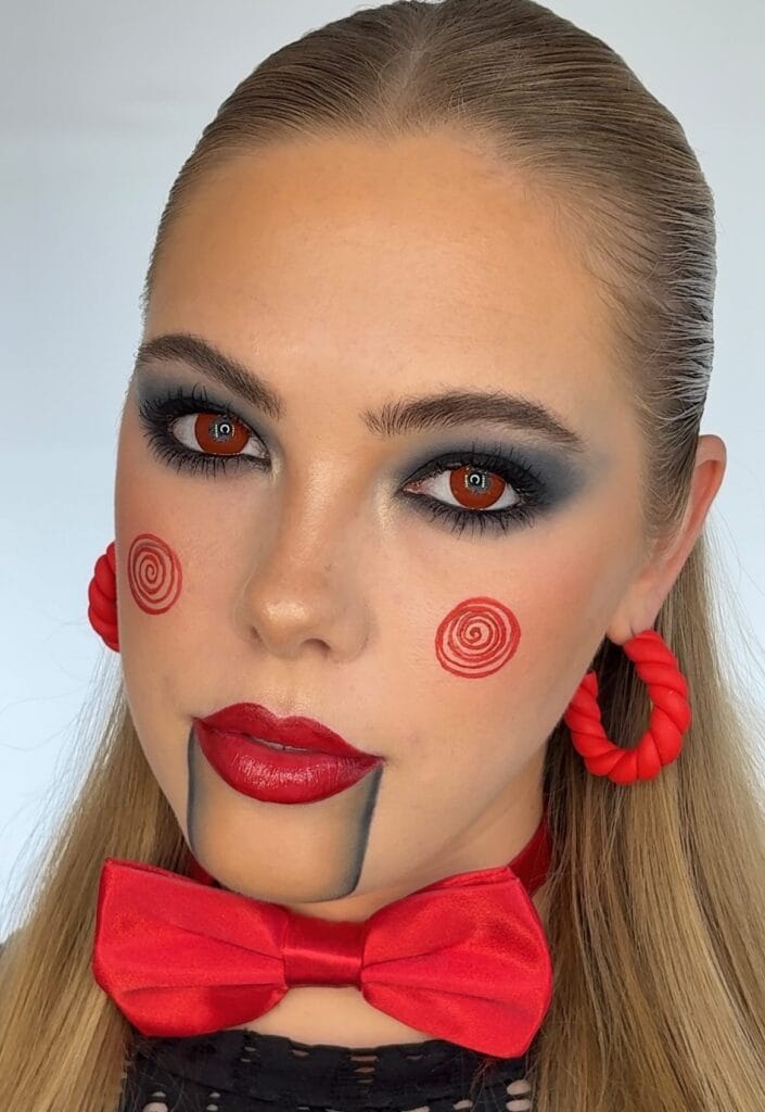 Halloween makeup with red spiral cheeks and black puppet lines for a Saw doll look.