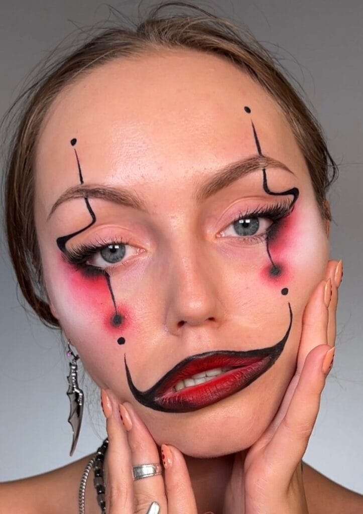 Modern clown Halloween makeup with graphic black lines, red blush, and bold lips.