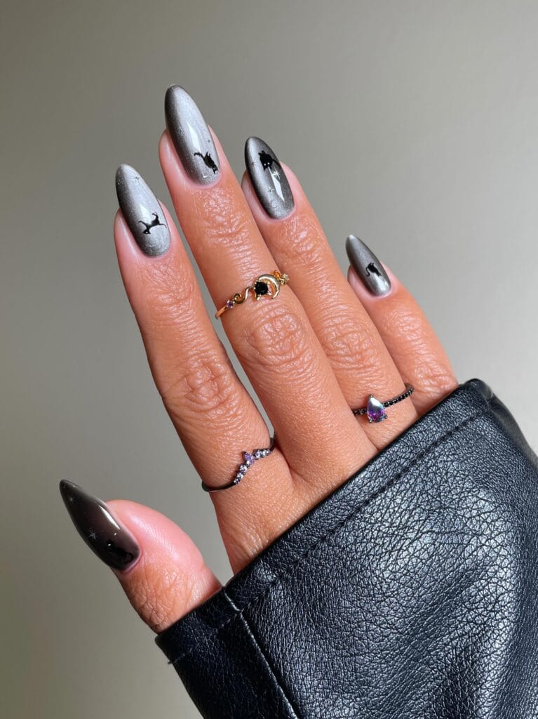 Silver chrome Halloween nails with black cat and moon accents on almond shape.
