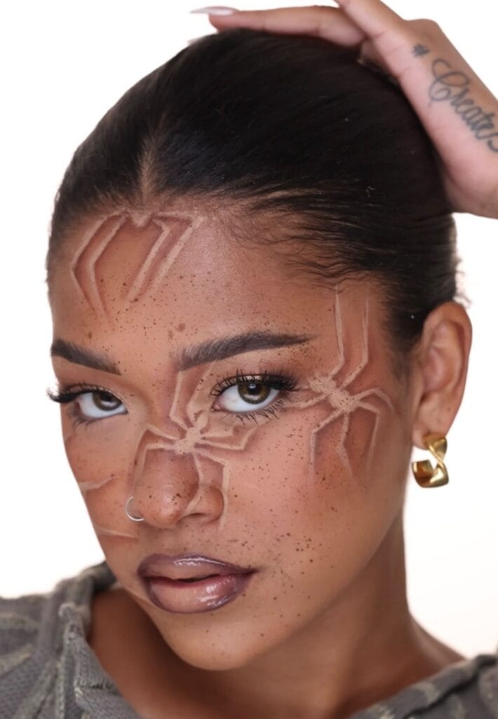 Halloween makeup with soft brown spider illusion design and nude lips.