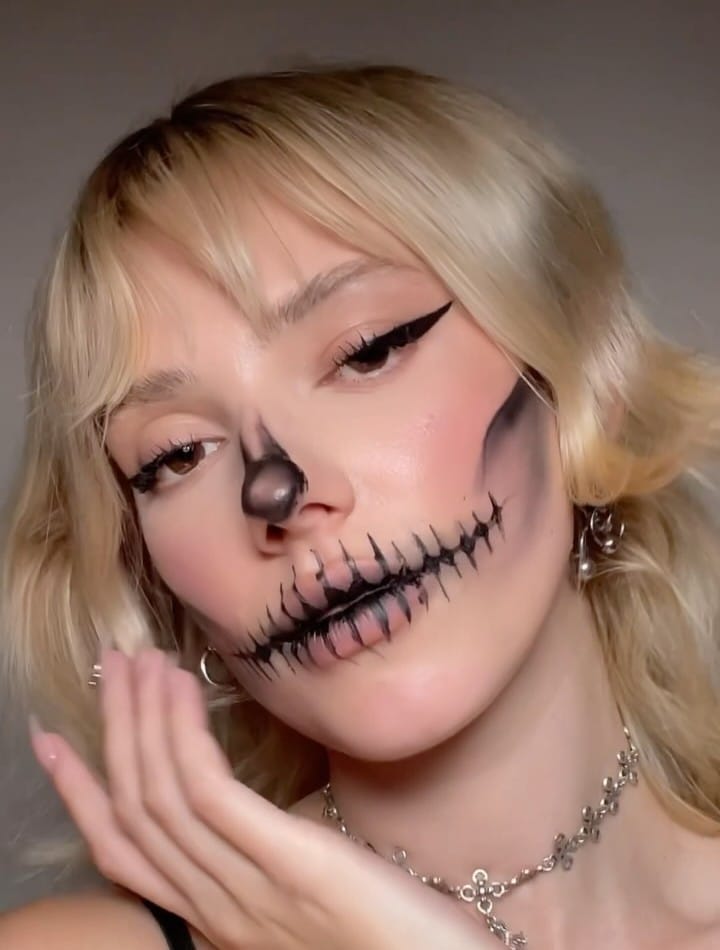Skeleton-inspired Halloween makeup with black stitches, black nose, and dramatic eyeliner.