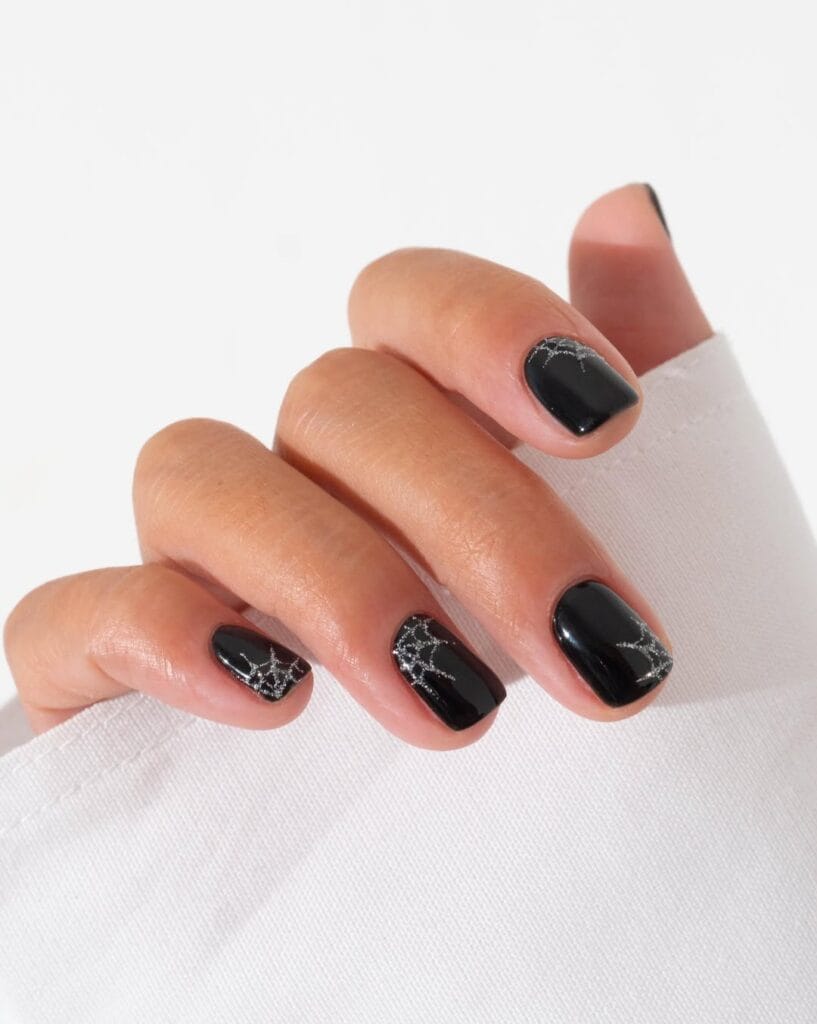  Short black Halloween nails with silver spiderweb glitter accents.
