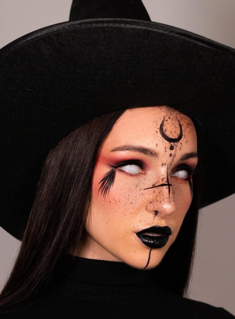Halloween makeup with crescent moon, black lipstick, and white contacts for a witchy look.