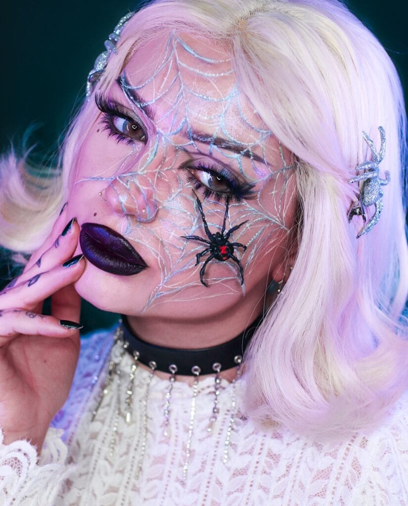 Spider queen Halloween makeup with frosted webs, dramatic lashes, and plum lips.
