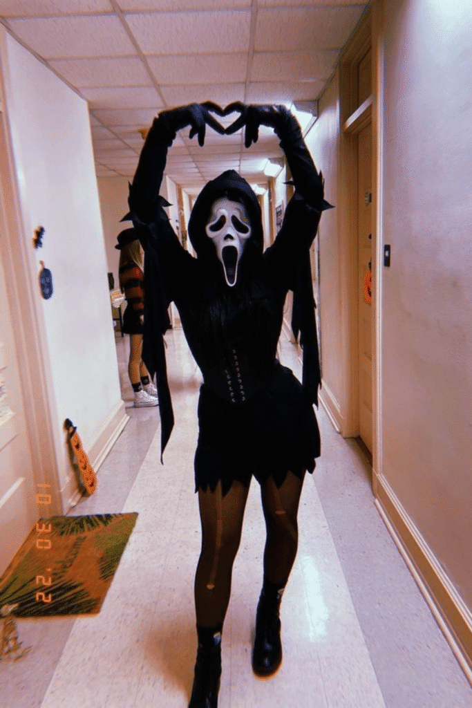 Halloween costume with black corset, Ghostface mask, and playful pose, a cute and spooky twist on the classic Scream Halloween look.