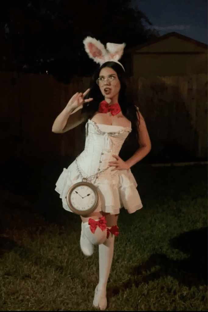 Halloween costume with white corset dress, bunny ears, red bows, and a clock, a playful and stylish take on the White Rabbit.

