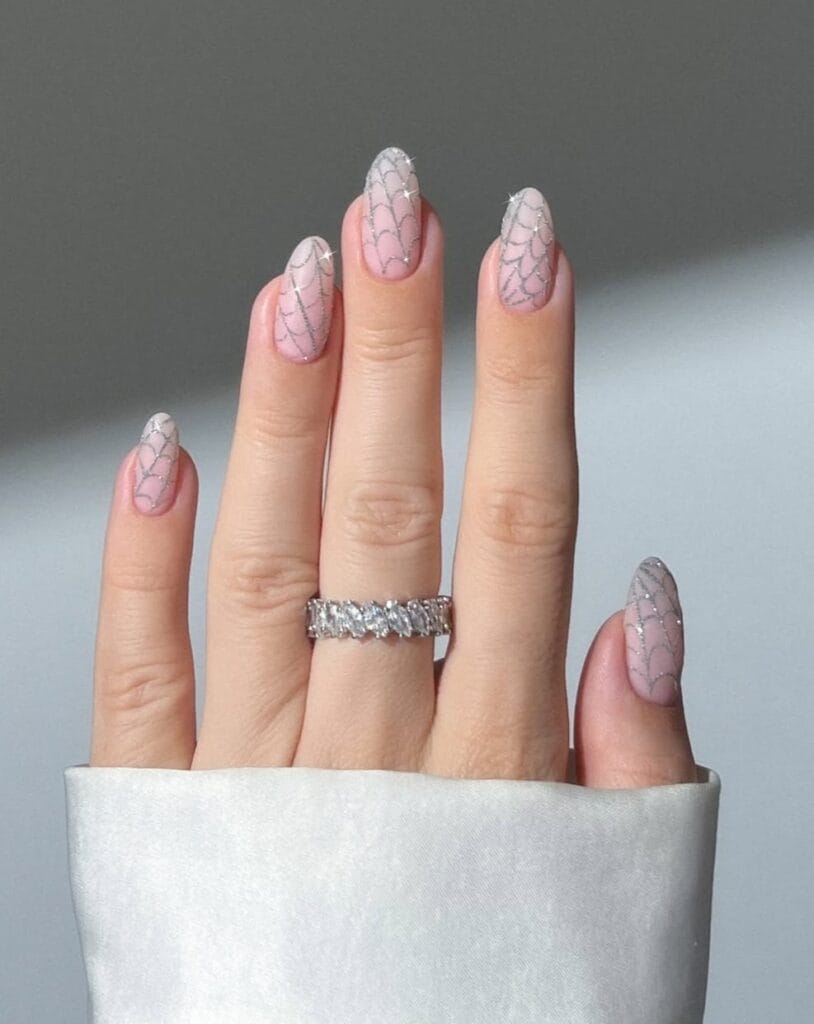 Pale pink almond nails with fine silver glitter spiderweb art for Halloween.
