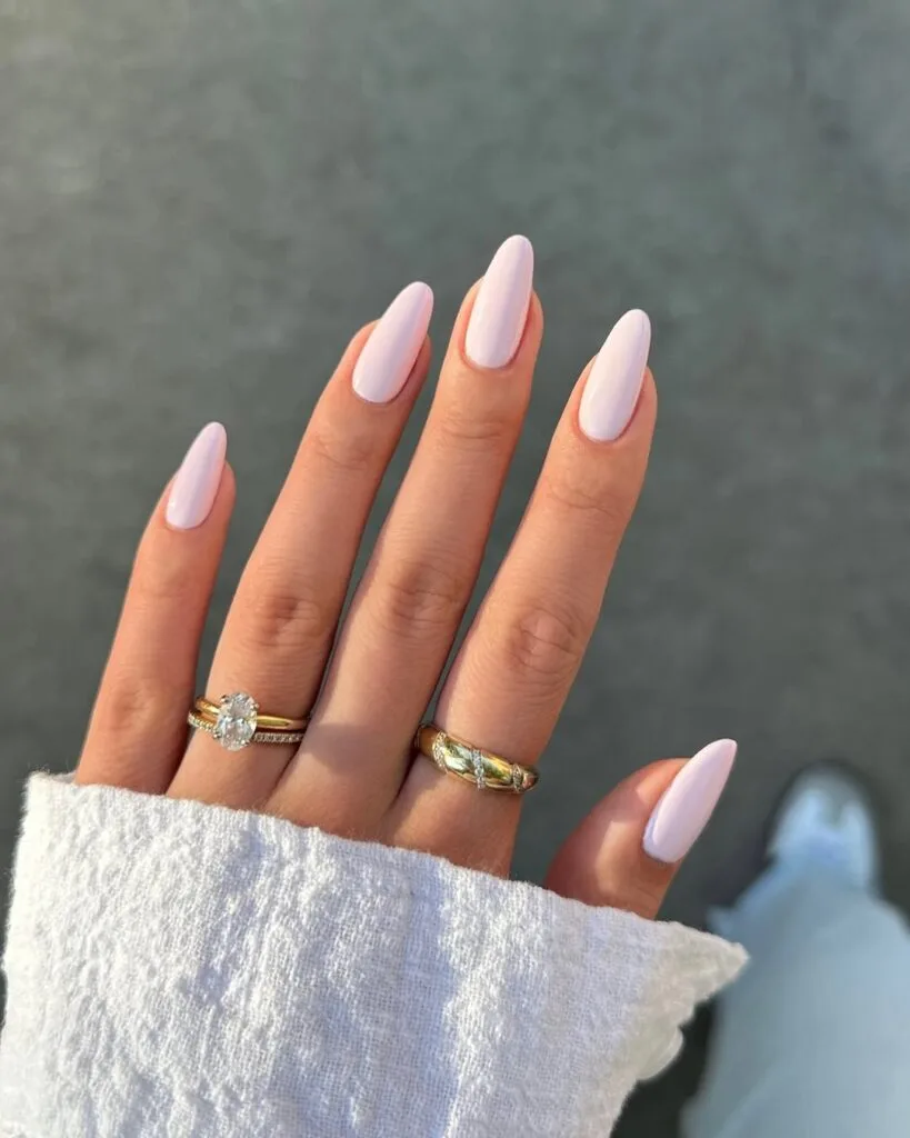 Light pink almond old money nails, soft and glossy, styled with gold rings for elegant look.