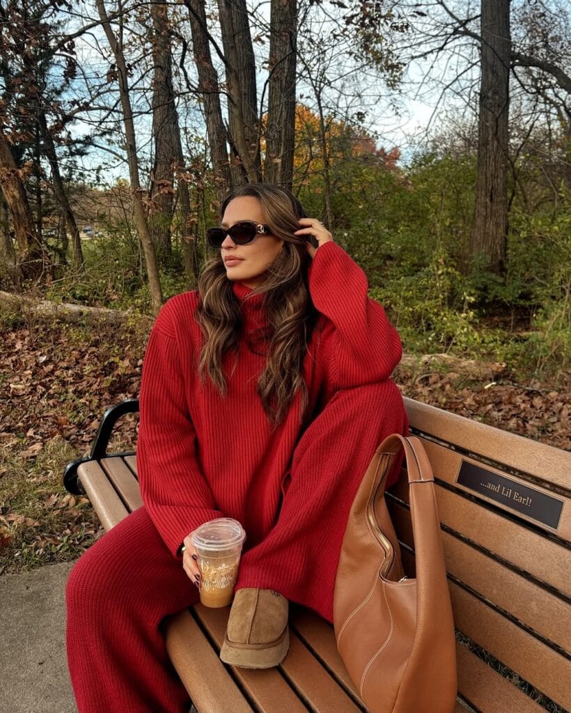 Woman in red knit set and Ugg boots, holding coffee on park bench; stylish Ugg outfit for winter.