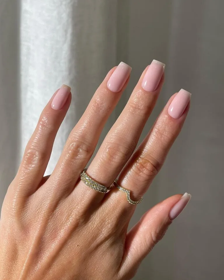 Blush pink neutral nails, medium square shape, glossy finish, styled with gold rings.