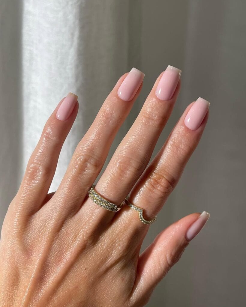 Blush pink neutral nails, medium square shape, glossy finish, styled with gold rings.