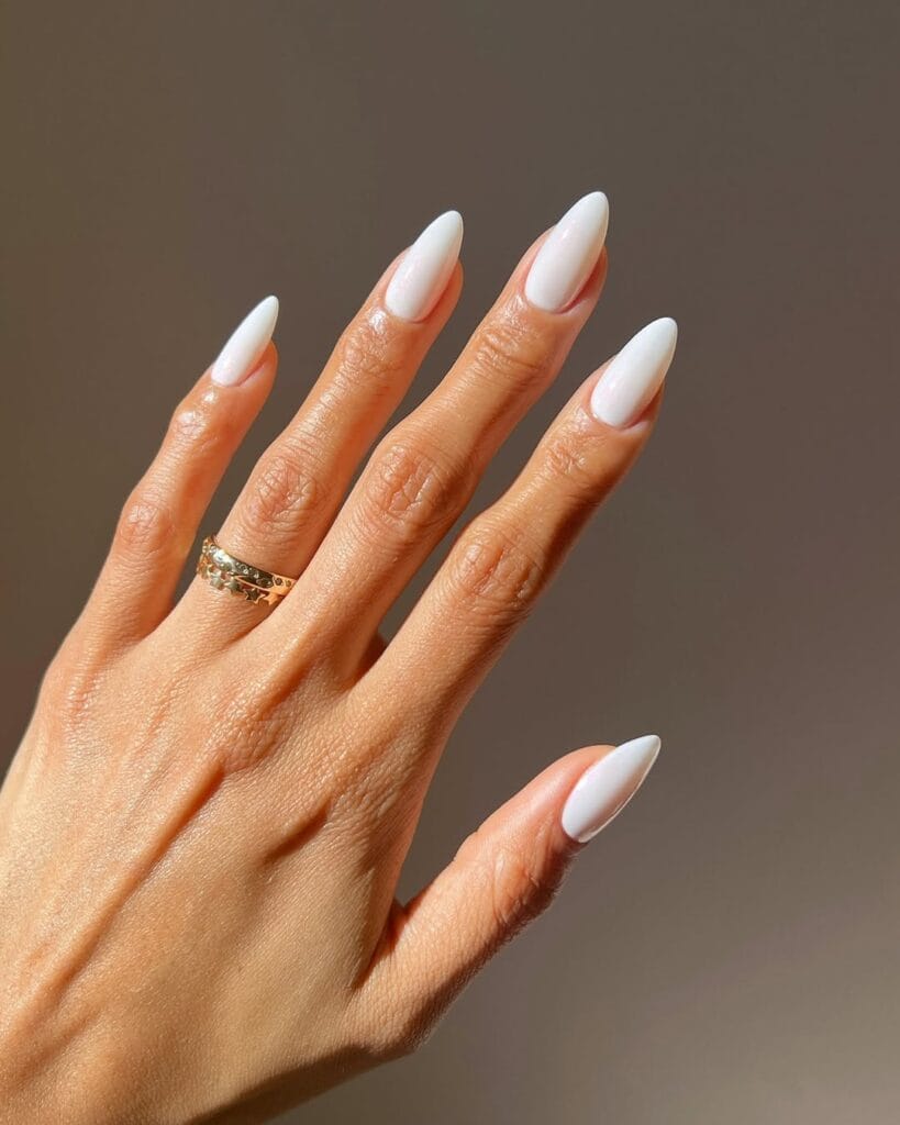 Almond-shaped old money nails in milky white, glossy finish, styled with gold ring.
