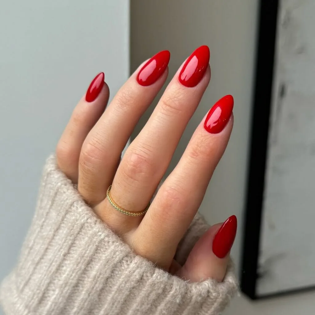 Glossy red old money nails, almond-shaped, paired with gold ring and beige sweater.