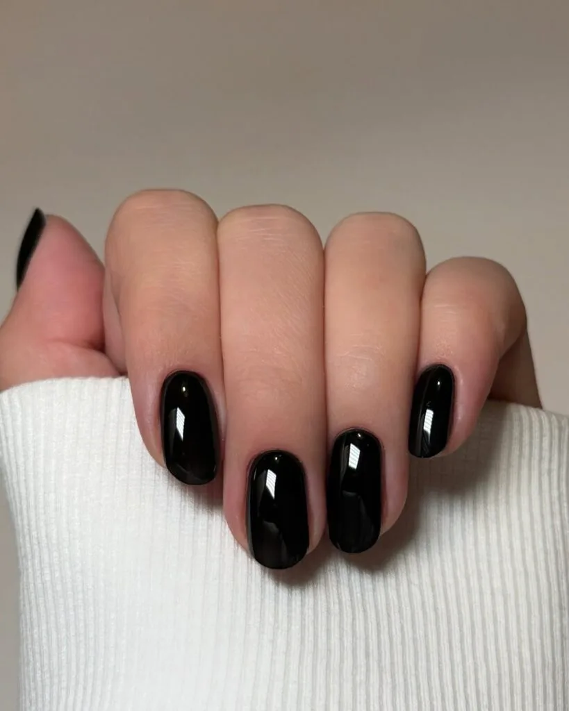 Short glossy black old money nails, rounded, styled with white ribbed sleeve.