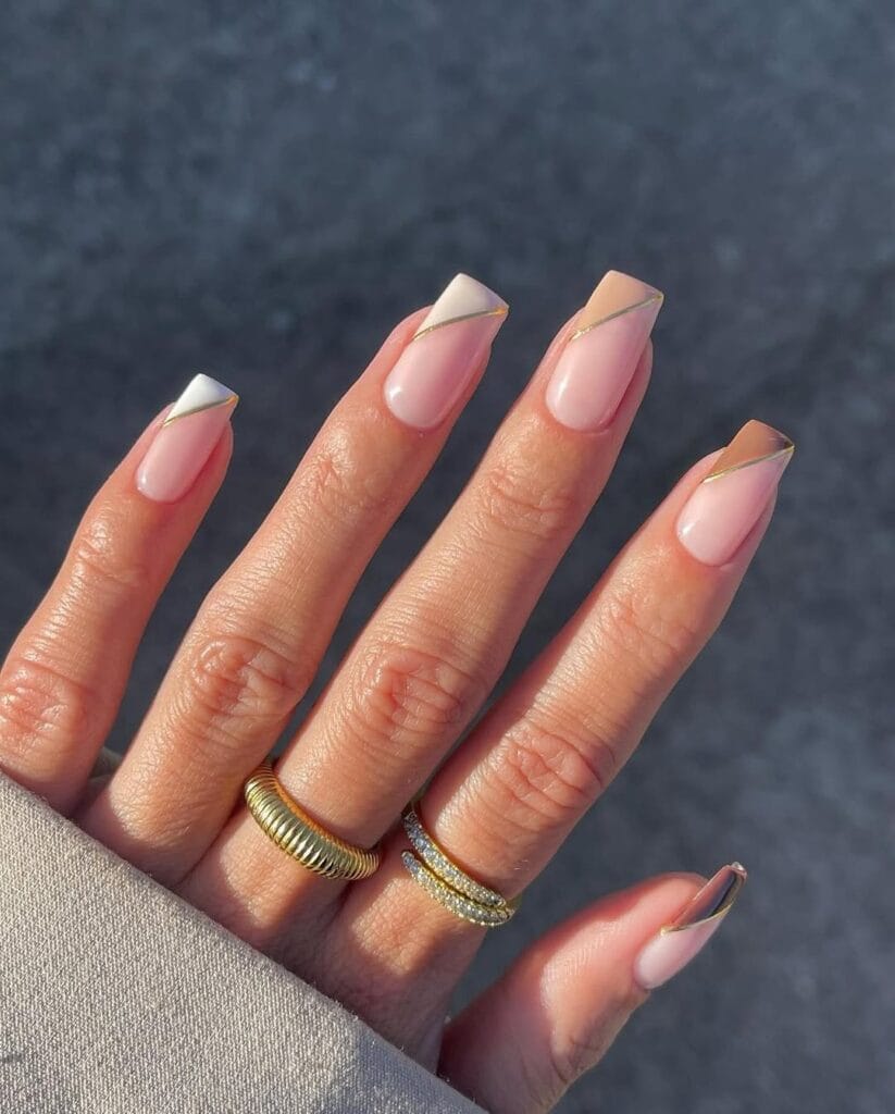 Neutral French tip nails with gold, angled abstract tips, nude base, modern square shape.
