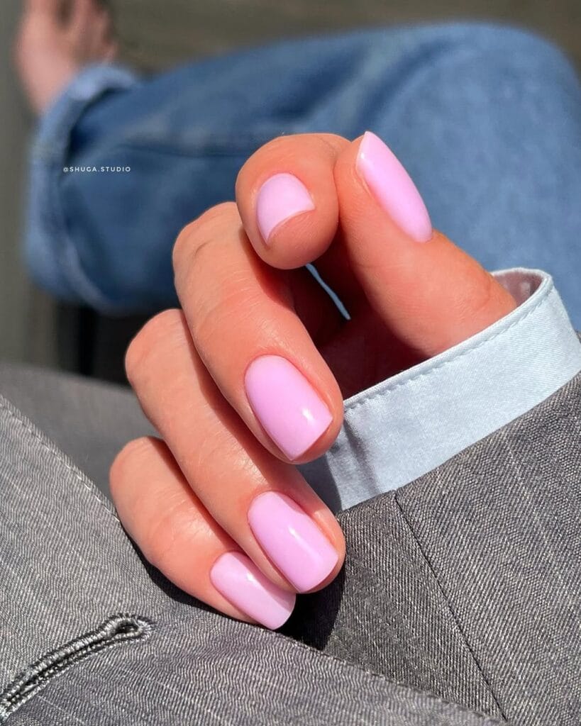 Soft pastel pink old money nails, short and shiny, paired with light blue shirt and grey blazer.
