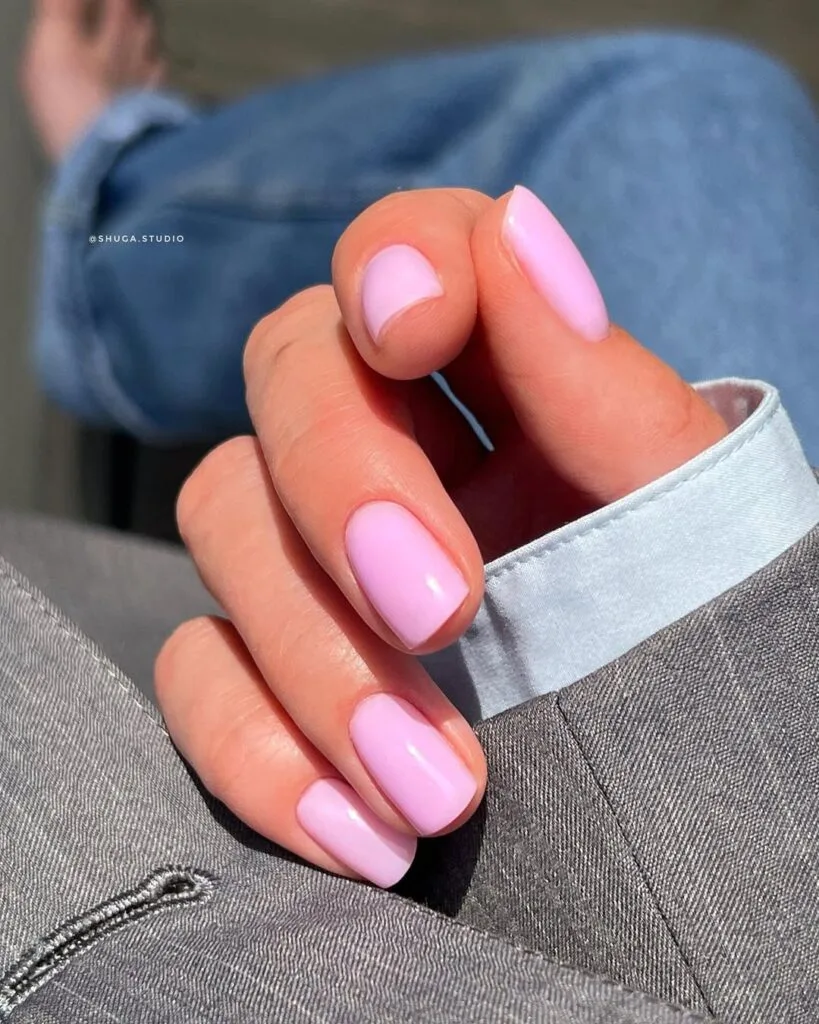 Soft pastel pink old money nails, short and shiny, paired with light blue shirt and grey blazer.