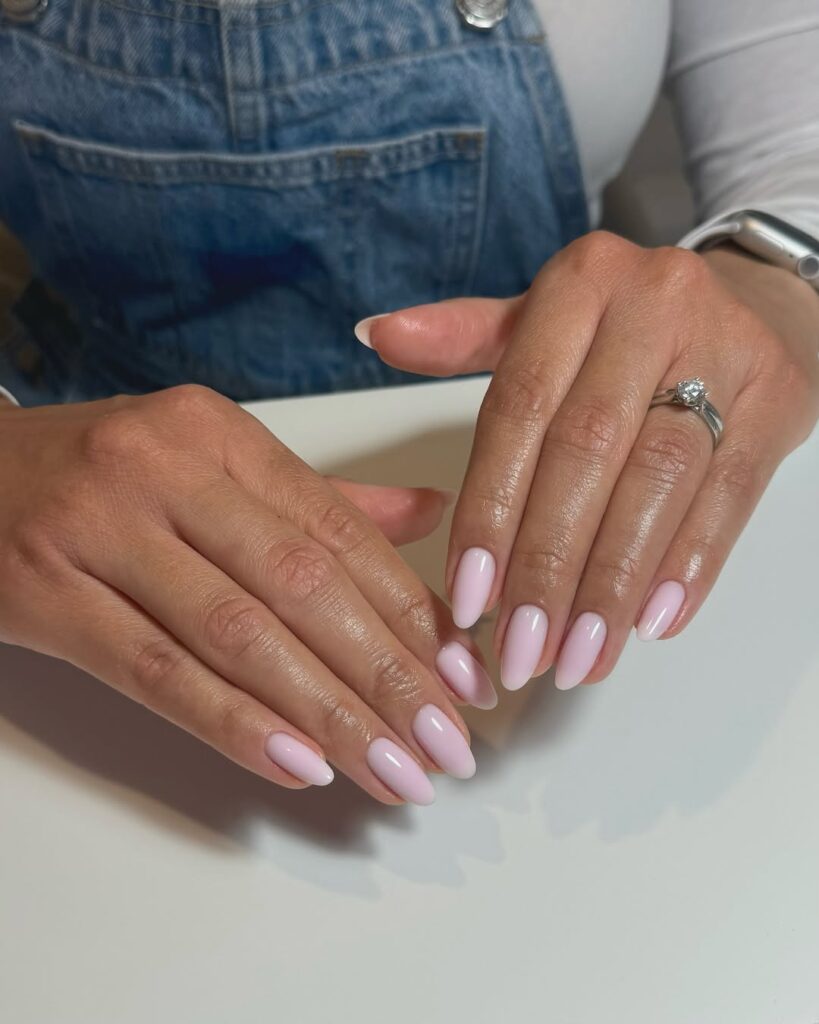 Pale pink almond neutral nails, glossy finish, styled with denim, fresh and effortless.