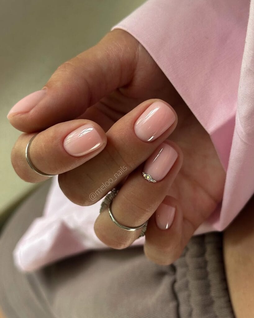 Short sheer peach pink neutral nails, minimal gem accent, glossy, clean and simple look.
