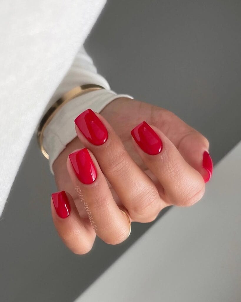 Cherry red square old money nails, glossy finish, styled with gold bracelet and white sleeve.
